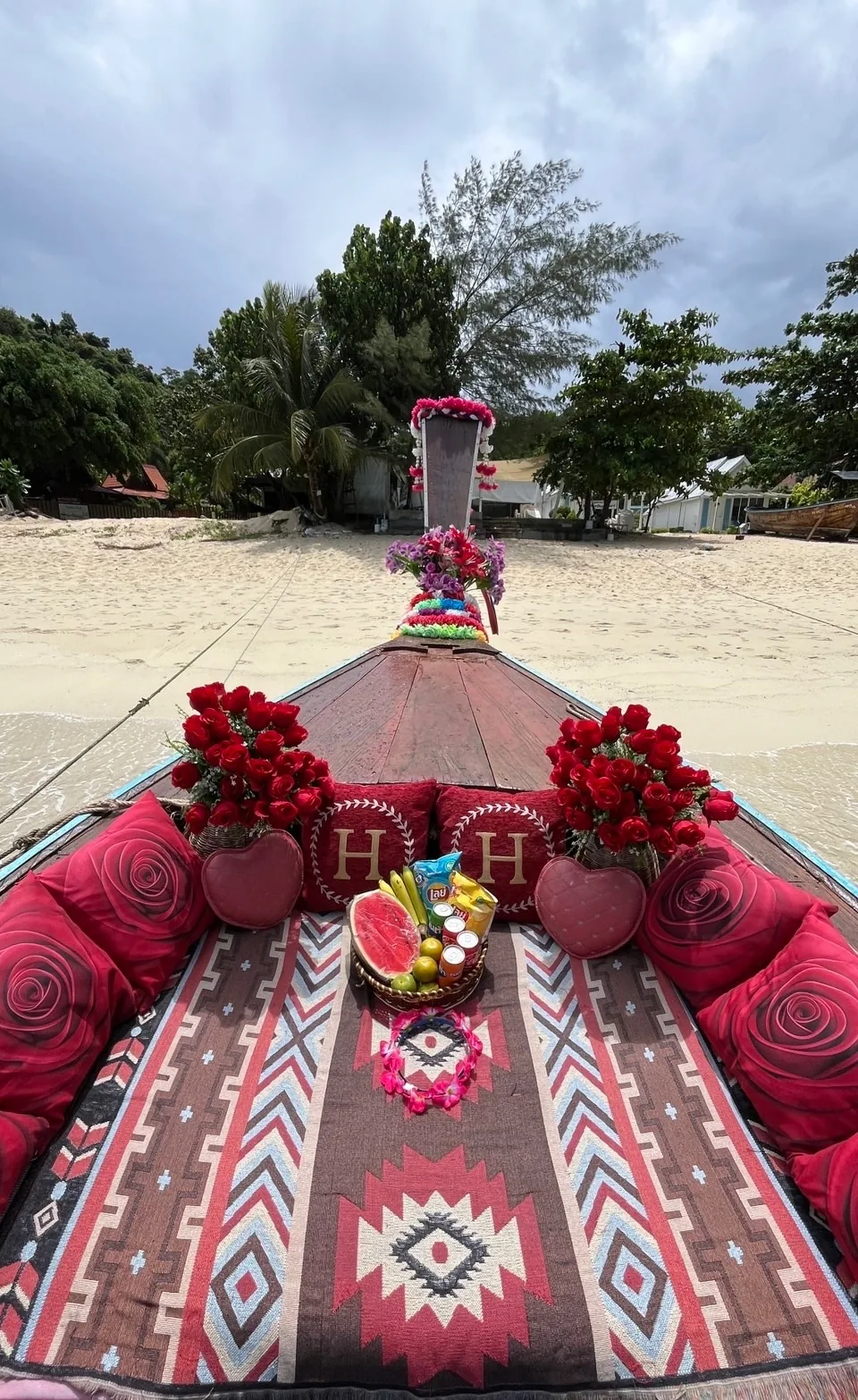 ถาดผลไม้และหมอนอักษรบนหัวเรือ มองเห็นชายหาดและแนวต้นไม้ด้านหน้า