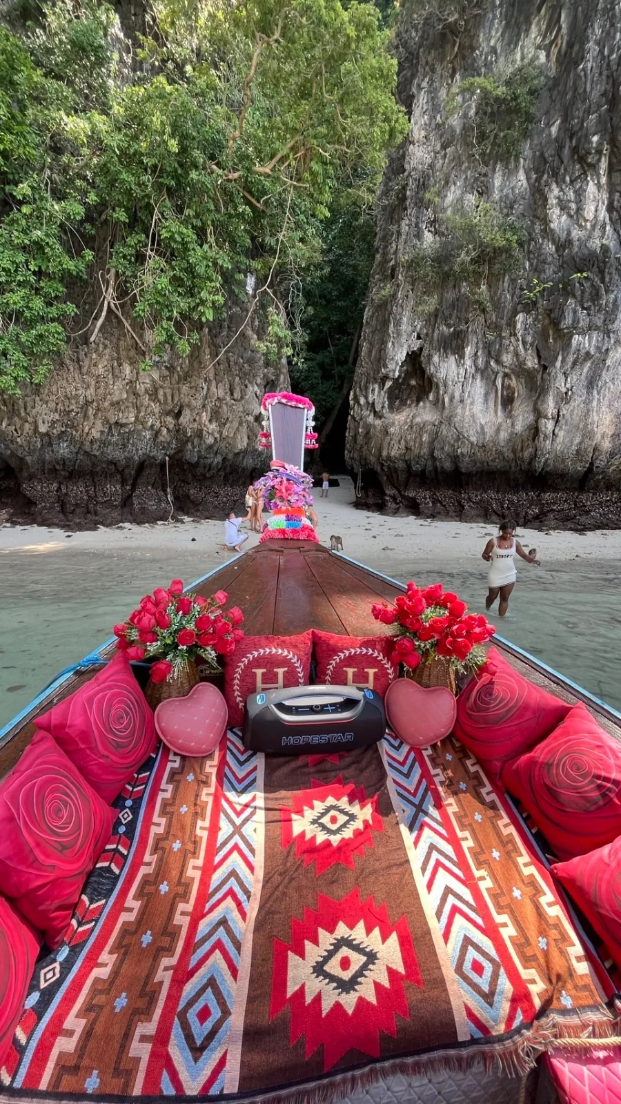 มุมมองจากหัวเรือหางยาวตกแต่งเต็มลำ กำลังแล่นเข้าหาดทรายที่มีผาหินปูนสูงขนาบสองข้าง