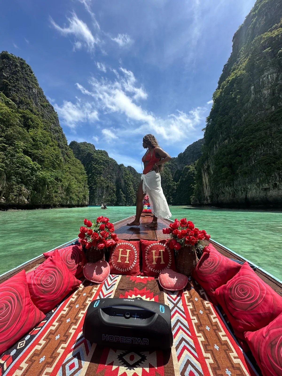A guest standing on the bow of a longtail boat in Pi-leh Lagoon, emerald water framed by limestone cliffs